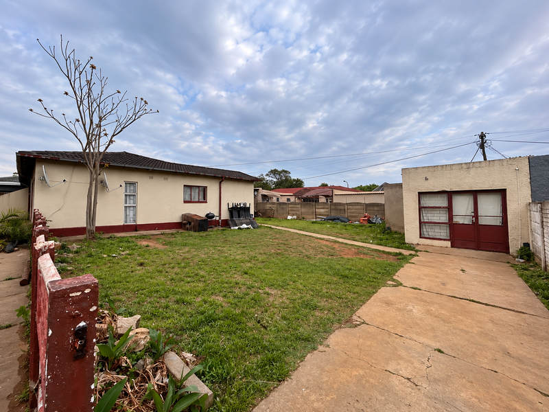 Rear view of the property featuring a spacious backyard, concrete driveway, and a detached garage with a tiled roof.