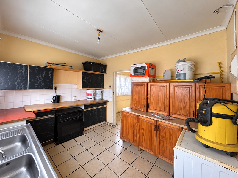 A dated kitchen featuring a mix of black and wood-finish cabinetry, tiled flooring, and a double bowl sink, requiring cosmetic updates and repairs.