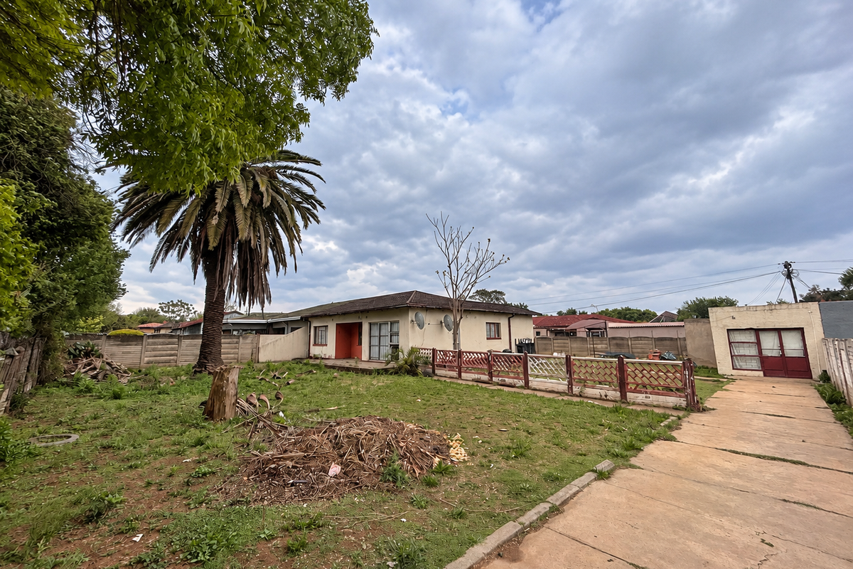 Rear view of the property featuring a large garden, concrete driveway, detached garage, and precast boundary walling.