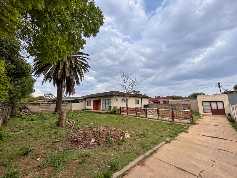 Rear view of the property featuring a large garden, concrete driveway, detached garage, and precast boundary walling.