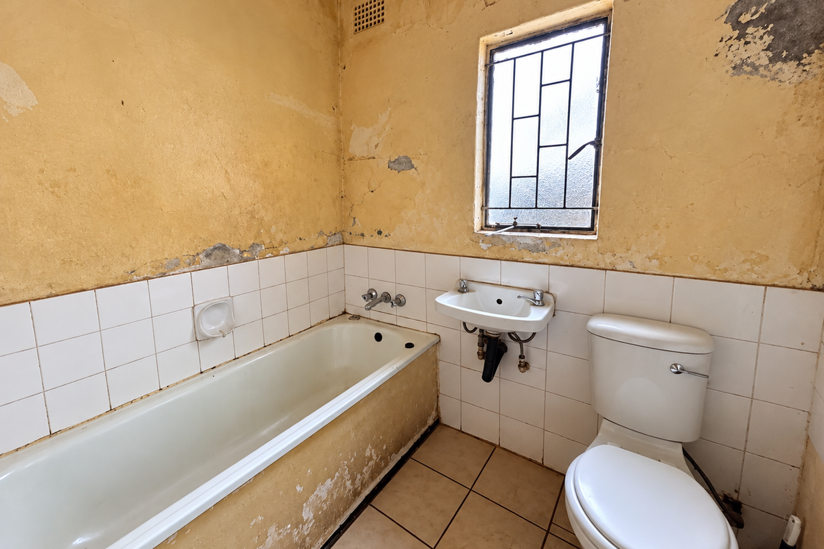 A dated bathroom featuring a bathtub, wall-mounted basin, and toilet, requiring significant renovation and cosmetic repairs to the walls and finishes.