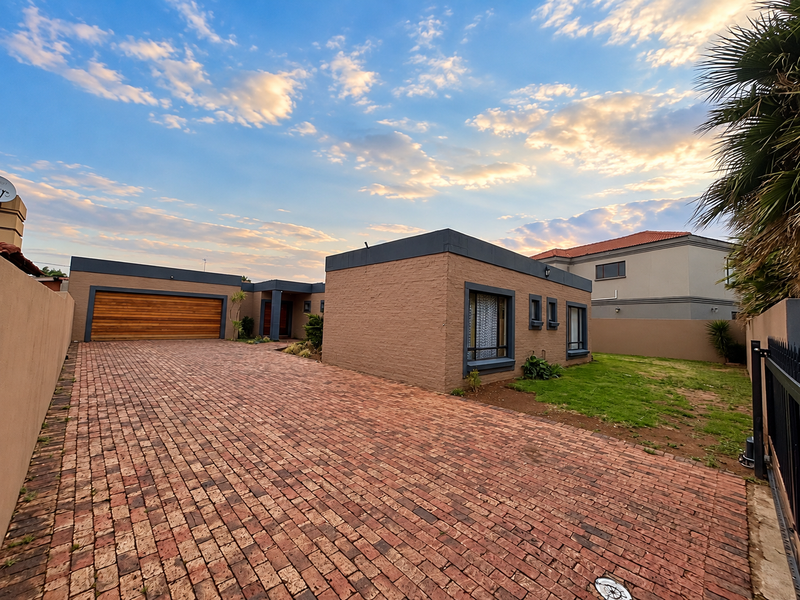 A well-maintained modern house featuring a spacious brick-paved driveway, a wooden garage door, and a clean painted brick exterior facade.