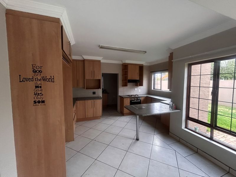 A functional kitchen featuring built-in wooden cabinetry, a built-in oven with hob, tiled flooring, and a breakfast nook area with natural light.