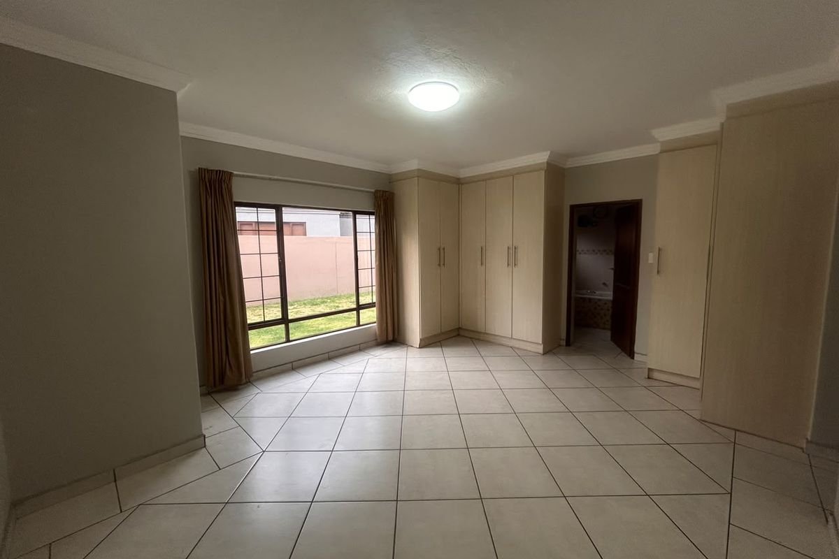 Spacious bedroom featuring neutral tiled flooring, extensive built-in cupboard storage, and a large window providing natural light.