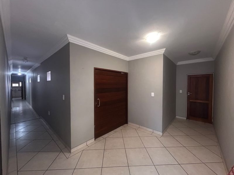 A spacious, well-lit hallway featuring neutral grey walls, tiled flooring, and classic crown molding, connecting multiple rooms within the home.
