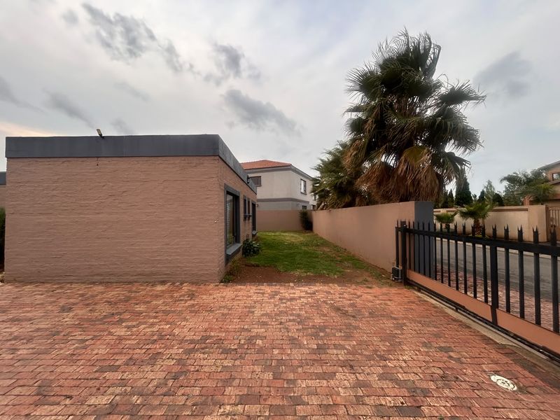 Front exterior view of the property featuring a brick-paved driveway, secure boundary wall, and sliding gate entrance.