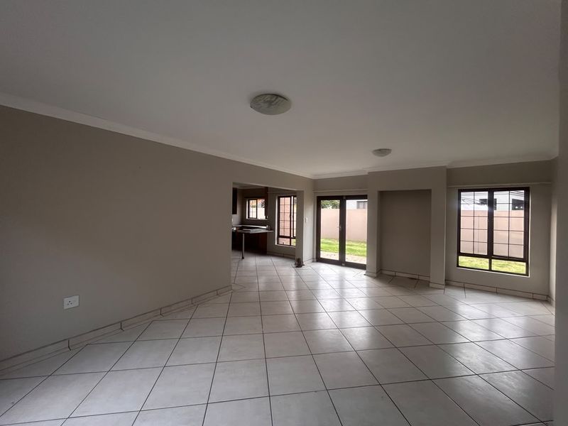 Spacious open-plan living area featuring neutral tiled flooring, large windows, and sliding glass doors providing access to the rear garden.
