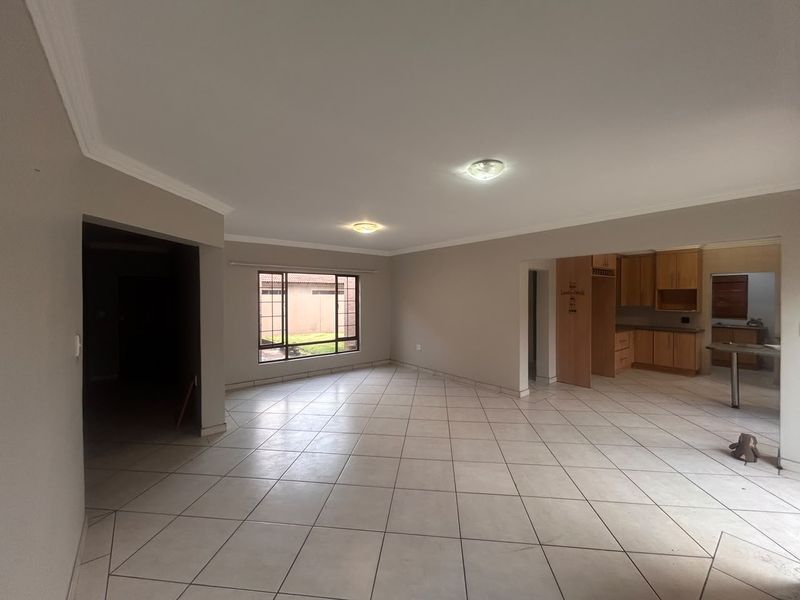 Spacious open-plan living area featuring neutral tiled flooring, coved ceilings, and an adjoining kitchen with built-in cabinetry.
