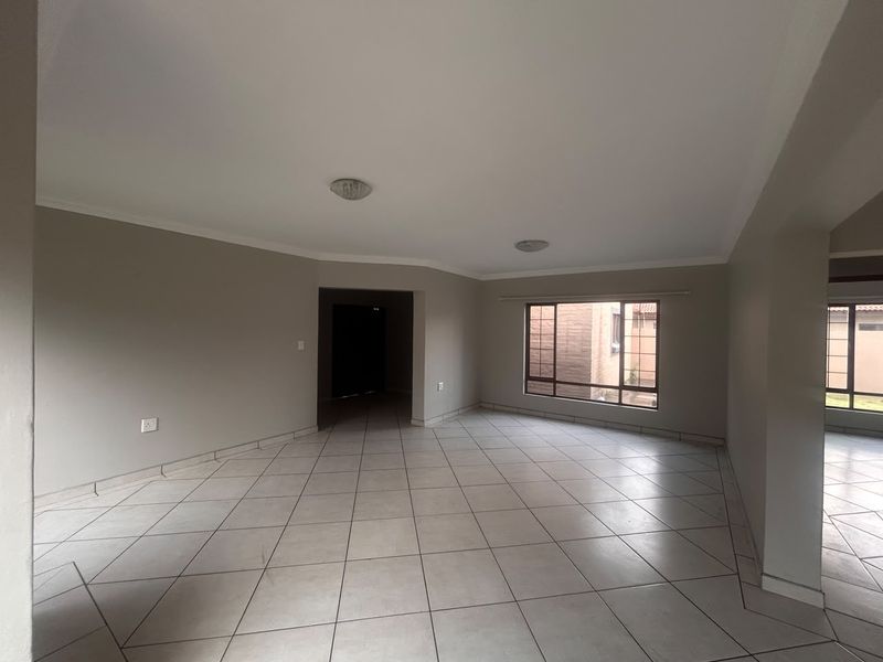 A spacious, empty living area featuring neutral wall tones, ceramic floor tiles, and large windows with security bars, offering a clean, blank canvas.