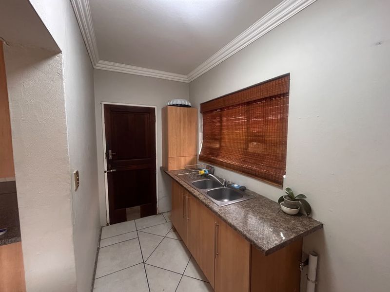 A functional scullery area featuring laminate cabinetry, granite countertops, a double basin sink, and tiled flooring.