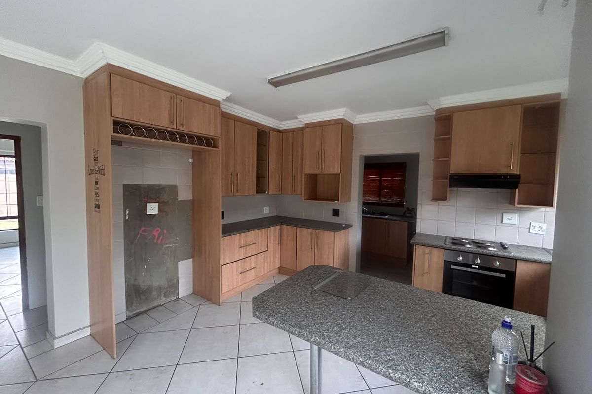A spacious kitchen featuring wooden cabinetry, granite countertops, and a breakfast nook. The space requires cosmetic repairs to the wall and tiling.