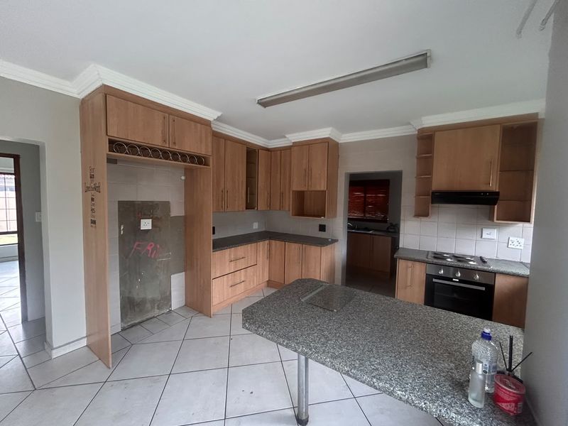 A spacious kitchen featuring wooden cabinetry, granite countertops, and a breakfast nook. The space requires cosmetic repairs to the wall and tiling.