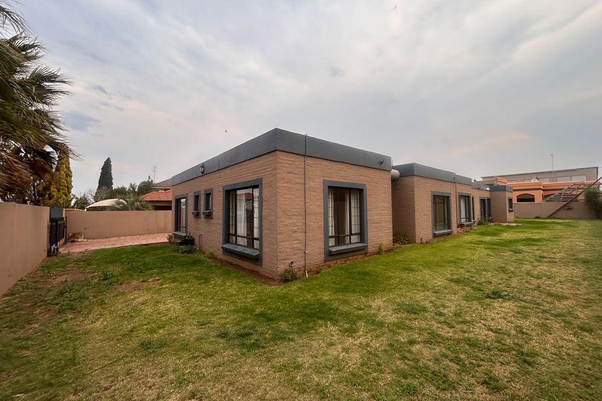 Rear view of the property featuring a brick facade, flat roof design, and a spacious surrounding lawn area.
