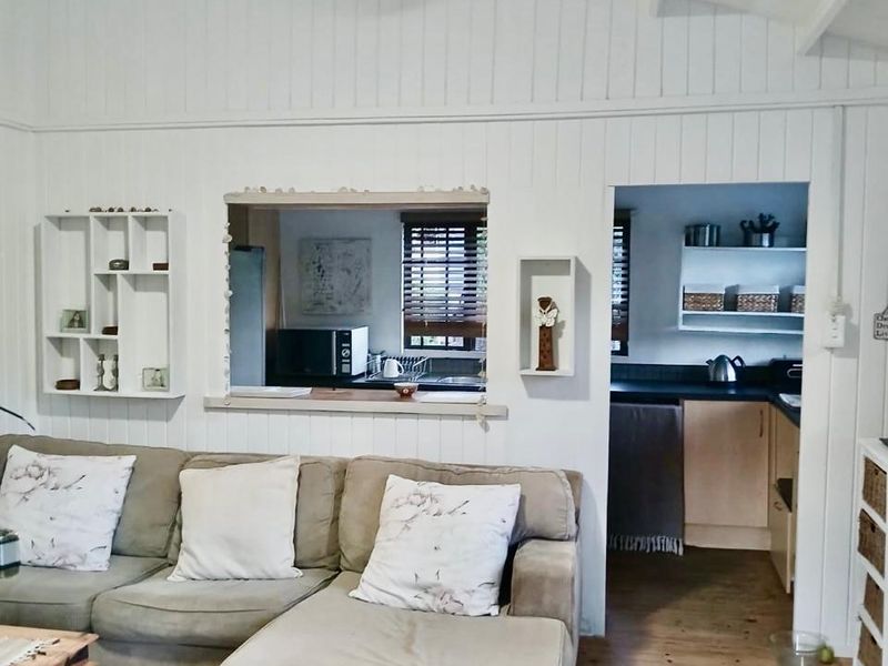 Open plan living area featuring timber flooring, exposed beam ceiling with fan, and a convenient pass-through window connecting to the adjacent scullery area.