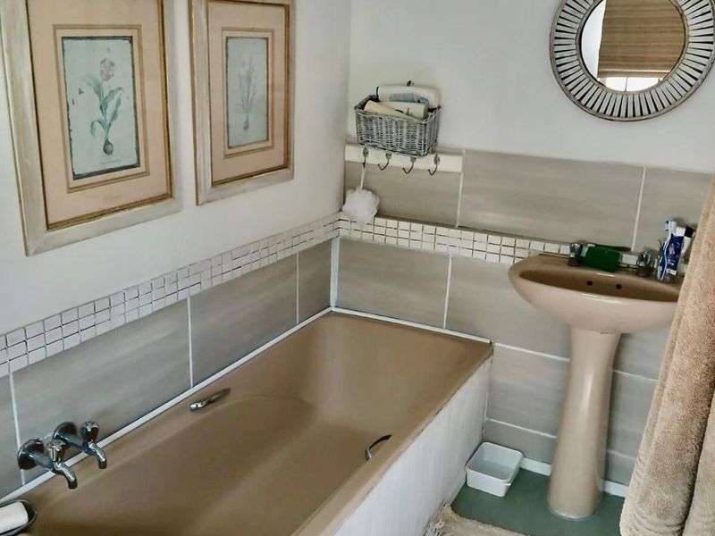 A functional bathroom featuring a neutral tiled splashback, a pedestal basin, and a built-in bathtub with chrome fixtures.