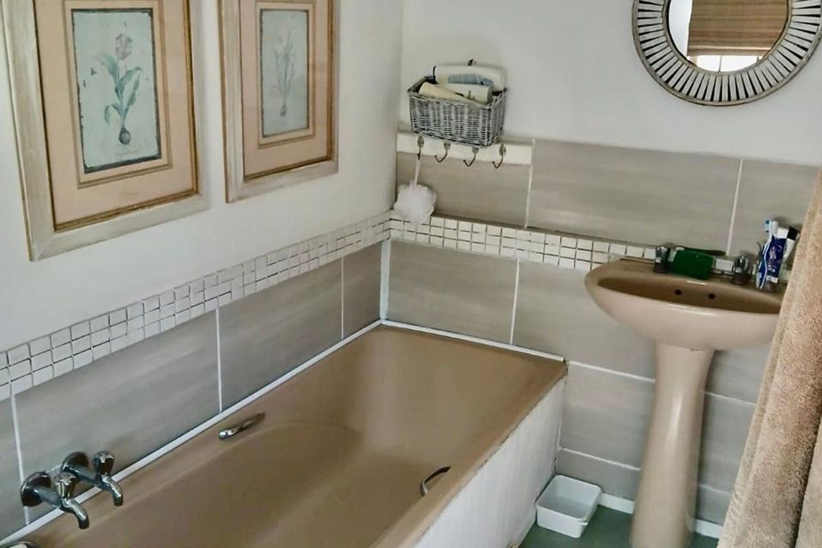 A functional bathroom featuring a neutral tiled splashback, a pedestal basin, and a built-in bathtub with chrome fixtures.