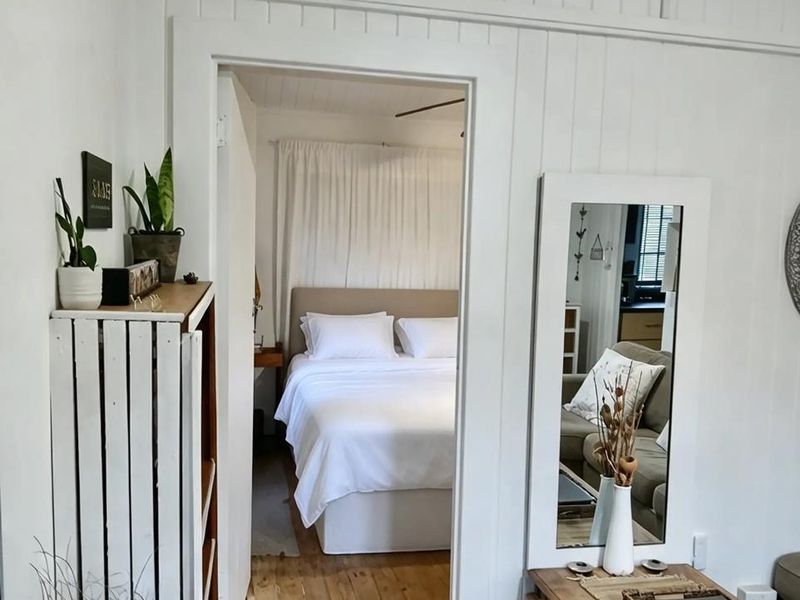 A view from a living area into a bedroom featuring classic timber flooring and white vertical wall paneling.