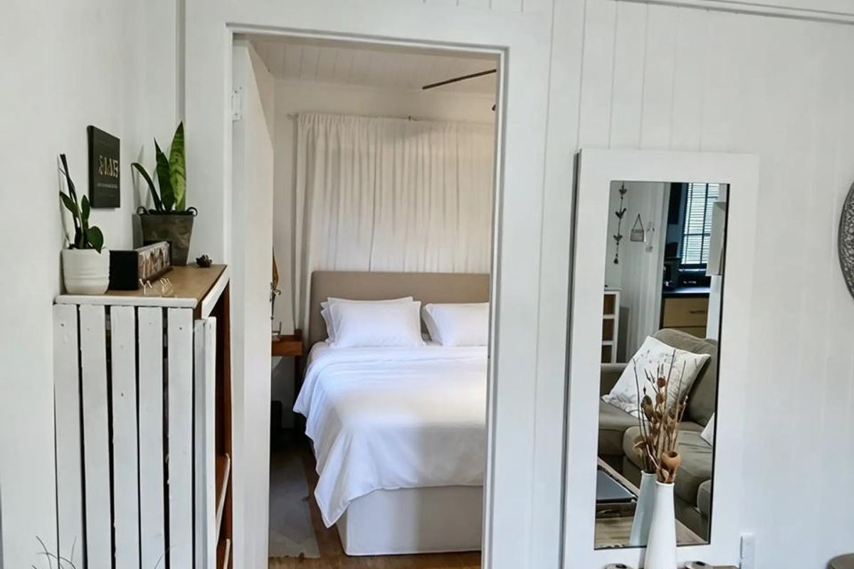 A view from a living area into a bedroom featuring classic timber flooring and white vertical wall paneling.