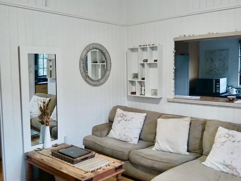 A cozy living room featuring timber flooring, white timber wall panelling, a ceiling fan, and a convenient serving hatch connecting to the kitchen area.