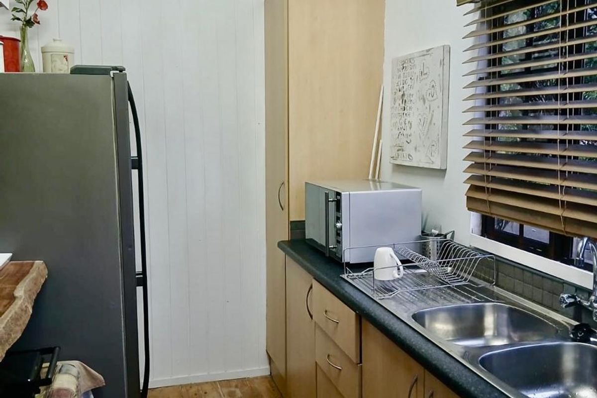 A functional kitchen featuring timber flooring, laminate cabinetry, a double bowl stainless steel sink, and vertical timber wall paneling.