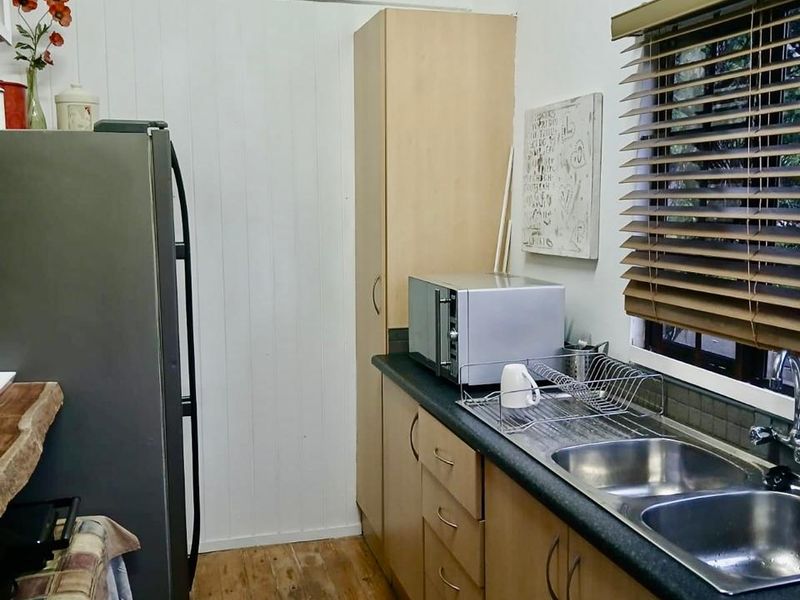 A functional kitchen featuring timber flooring, laminate cabinetry, a double bowl stainless steel sink, and vertical timber wall paneling.