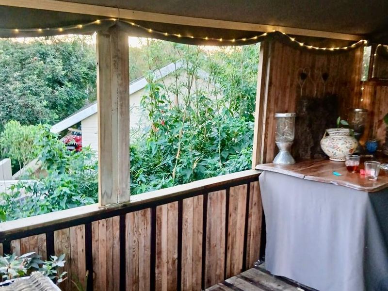 A rustic covered patio area featuring timber decking and a wooden balustrade, overlooking a lush garden setting.