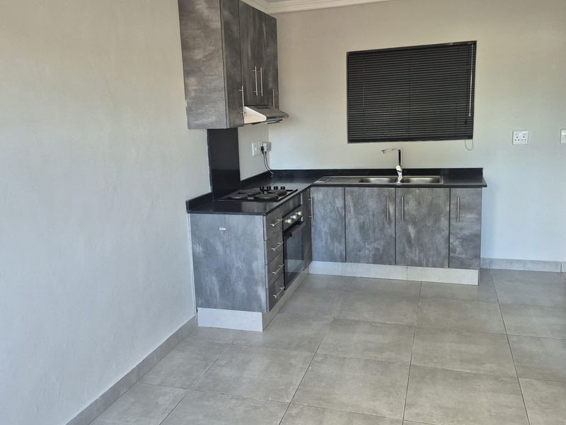 Modern kitchen featuring grey textured cabinetry, dark countertops, integrated oven and hob, stainless steel sink, and neutral tiled flooring.