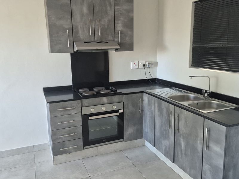 Modern kitchen featuring grey textured cabinetry, black countertops, integrated electric hob, oven, extractor fan, and a stainless steel sink with a mixer tap.