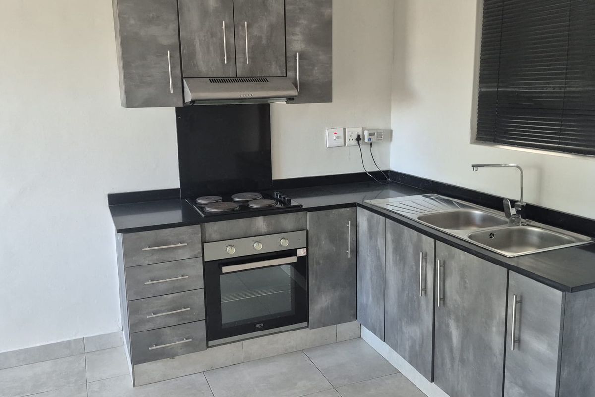 Modern kitchen featuring grey textured cabinetry, black countertops, integrated electric hob, oven, extractor fan, and a stainless steel sink with a mixer tap.