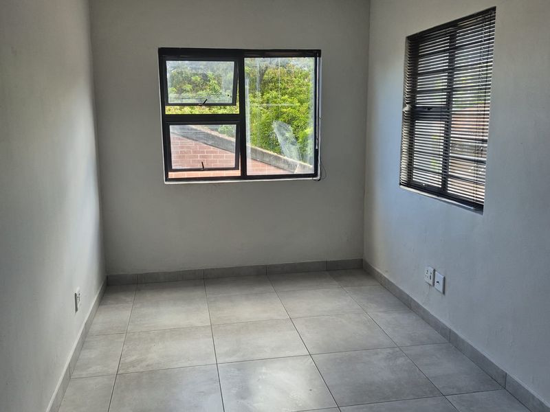 A bright, empty bedroom featuring neutral tiled flooring, clean walls, and aluminium-framed windows with fitted blinds.