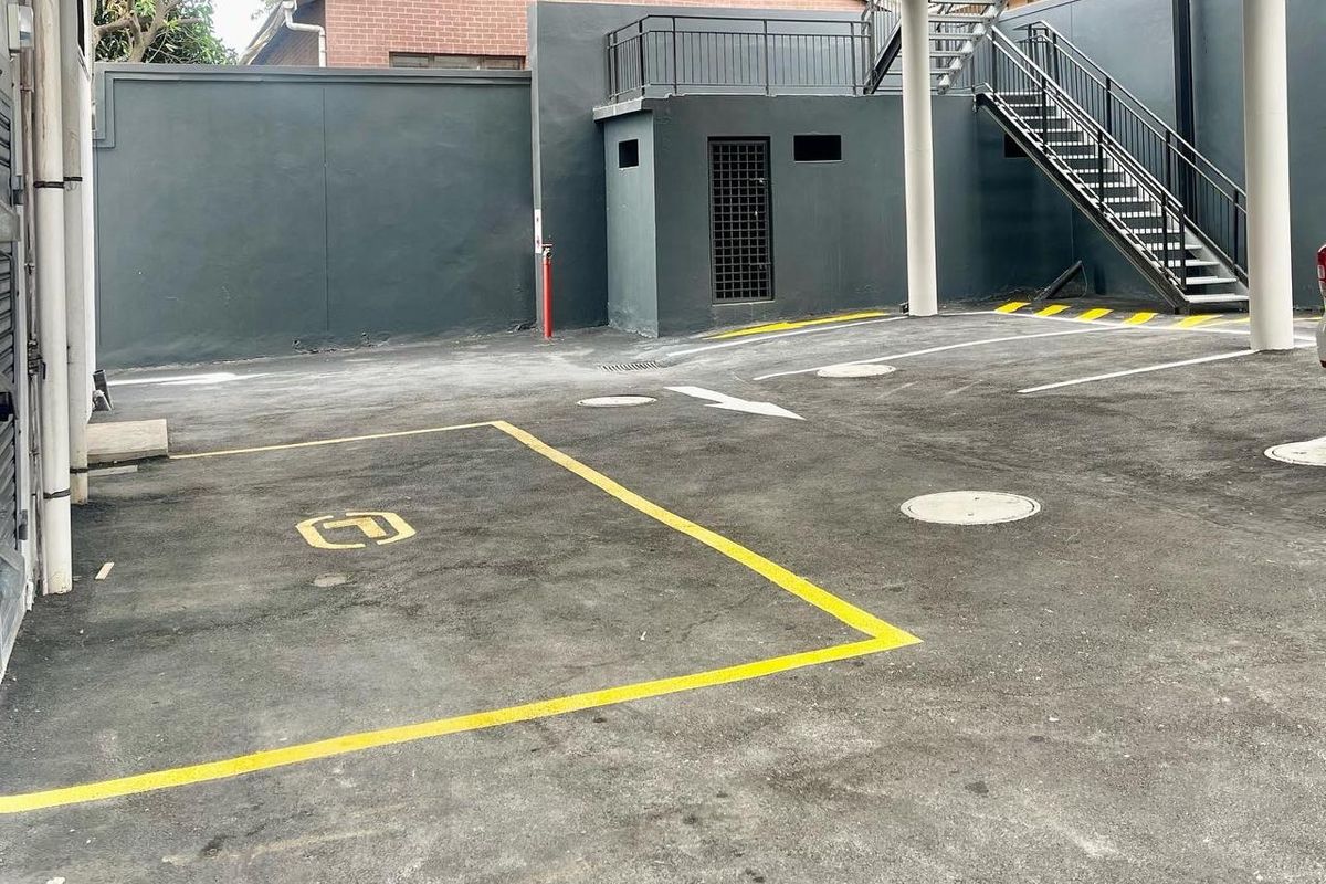 A covered parking area featuring concrete pillars, asphalt paving with marked bays, and an external metal staircase leading to an upper level.