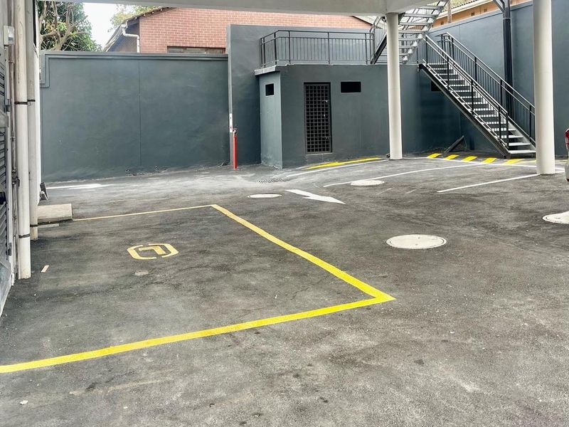 A covered parking area featuring concrete pillars, asphalt paving with marked bays, and an external metal staircase leading to an upper level.