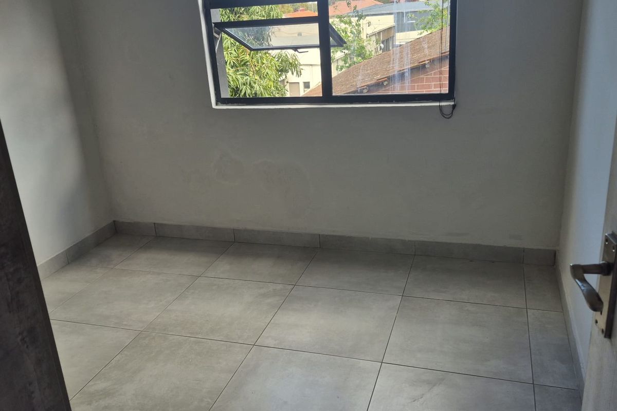 An empty bedroom featuring neutral tiled flooring and an aluminium window frame, offering a blank canvas for potential interior design and furnishing.
