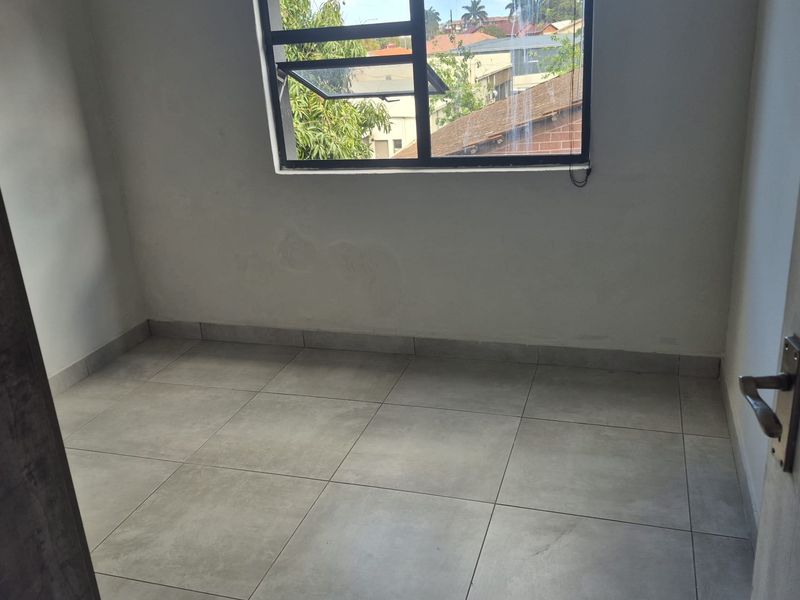 An empty bedroom featuring neutral tiled flooring and an aluminium window frame, offering a blank canvas for potential interior design and furnishing.