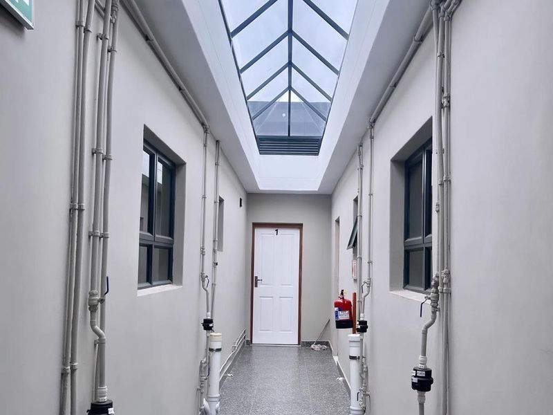 A bright, well-lit hallway featuring a large overhead skylight, tiled flooring, and exposed utility piping with integrated water meters.