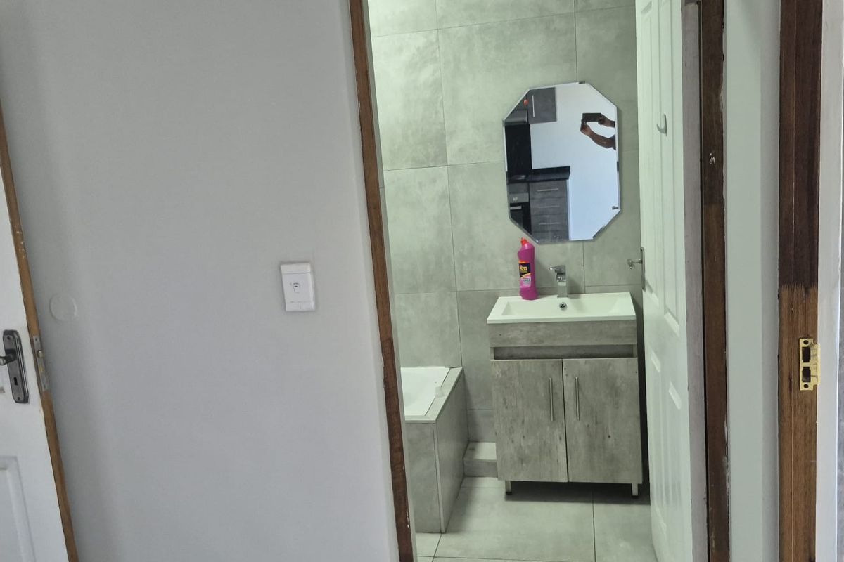 A compact bathroom featuring modern grey wall and floor tiles, a vanity cabinet with basin, and a bathtub.