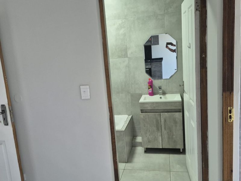 A compact bathroom featuring modern grey wall and floor tiles, a vanity cabinet with basin, and a bathtub.