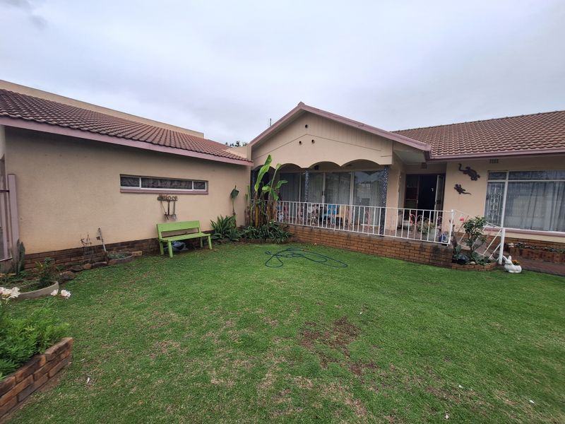 Rear view of the house featuring a covered patio, brick facade, tiled roof, and a well-maintained lawn area.