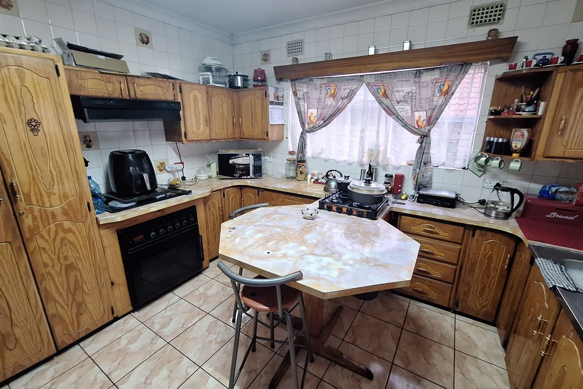 A dated kitchen featuring traditional wooden cabinetry, tiled backsplash, and tiled flooring, offering a functional layout with potential for modern renovation.