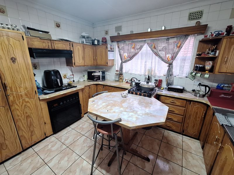 A dated kitchen featuring traditional wooden cabinetry, tiled backsplash, and tiled flooring, offering a functional layout with potential for modern renovation.