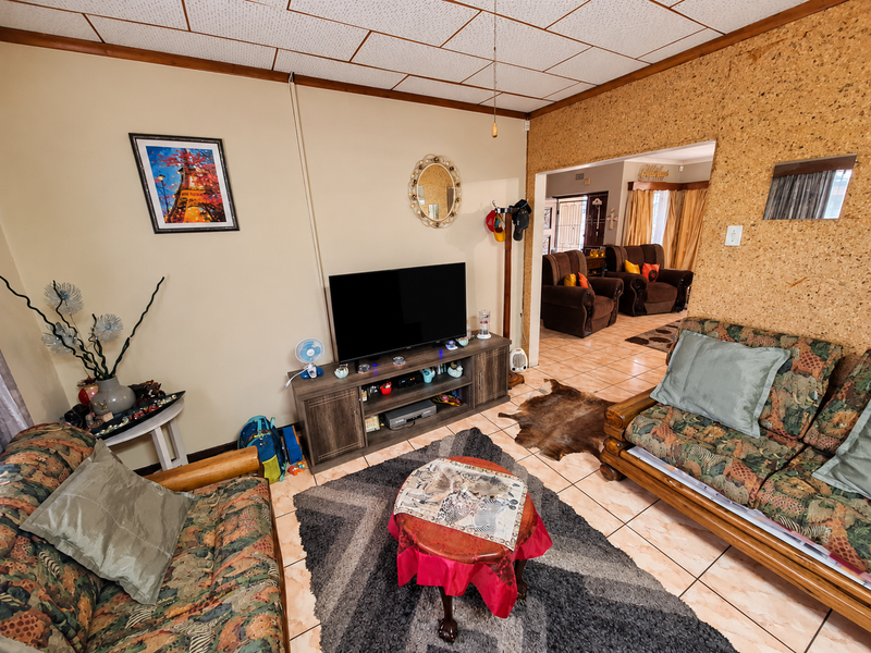 A living room featuring tiled flooring, cork wall paneling, and acoustic ceiling tiles, with an open archway leading to an adjacent living space.