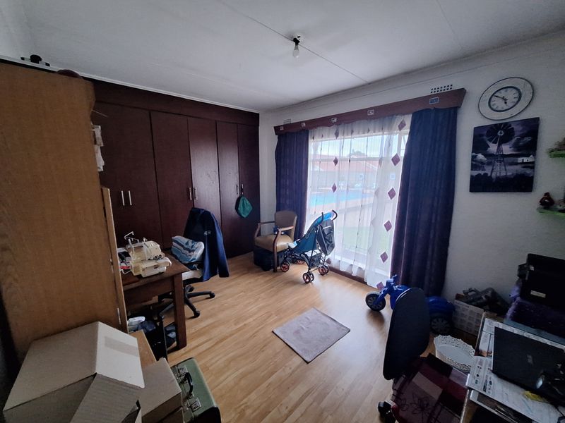 A bedroom featuring laminate flooring and extensive built-in wooden cupboards, offering ample storage space and natural light through the window.