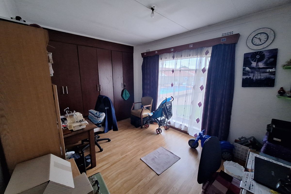 A bedroom featuring laminate flooring and extensive built-in wooden cupboards, offering ample storage space and natural light through the window.