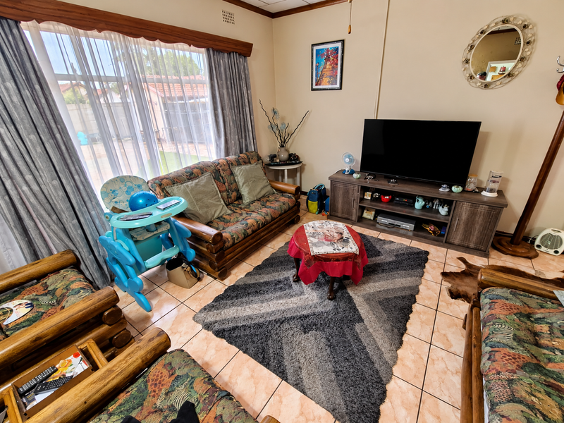 A comfortable living room featuring tiled flooring and a large window with curtain rails, providing natural light to the space.