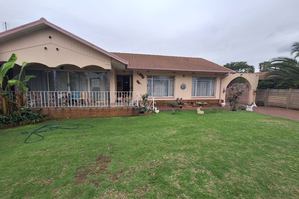 Rear view of a single-story house featuring a covered patio, tiled roof, and a spacious lawn with paved driveway and boundary wall.
