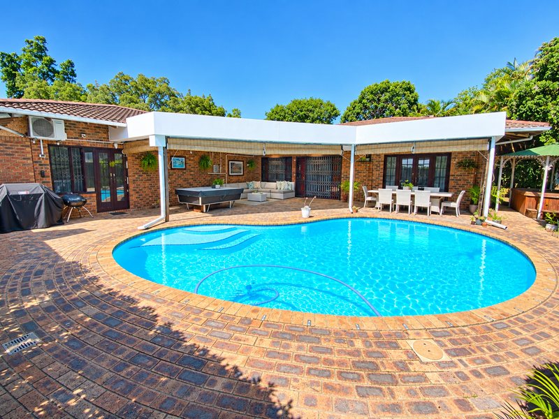 Spacious outdoor entertainment area featuring a large swimming pool, extensive brick paving, and a covered patio space ideal for hosting.