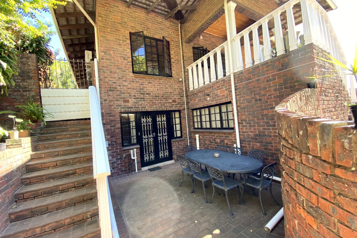Rear exterior view of a multi-level brick house featuring a paved patio area, balcony, and external brick staircase.