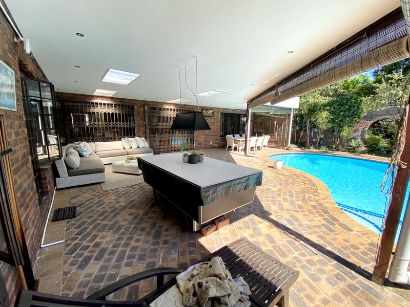 Spacious covered patio featuring brick paving, recessed lighting, and skylights, overlooking a private swimming pool and garden area.