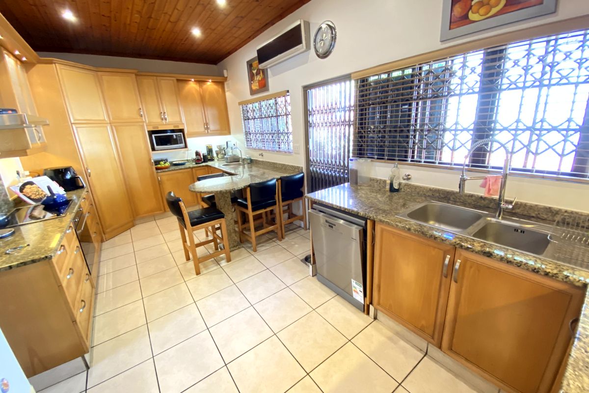 A functional kitchen featuring granite countertops, wooden cabinetry, tiled flooring, and a timber ceiling, equipped with built-in appliances and security features.