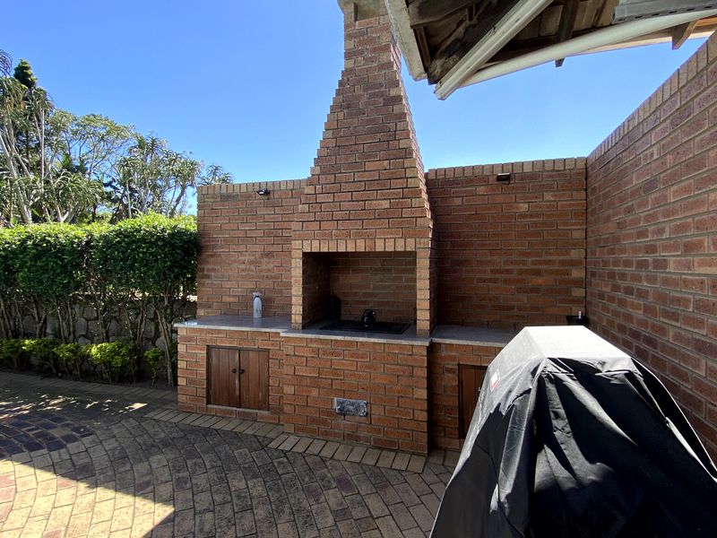 Outdoor patio area featuring a substantial built-in brick braai with stone countertops and integrated storage cabinetry, set on a paved surface.